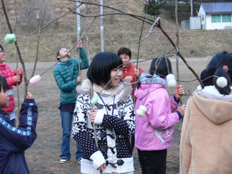 子どもたちがどんどん焼きに参加した様子（繭玉のお餅をつけた木を持っている）