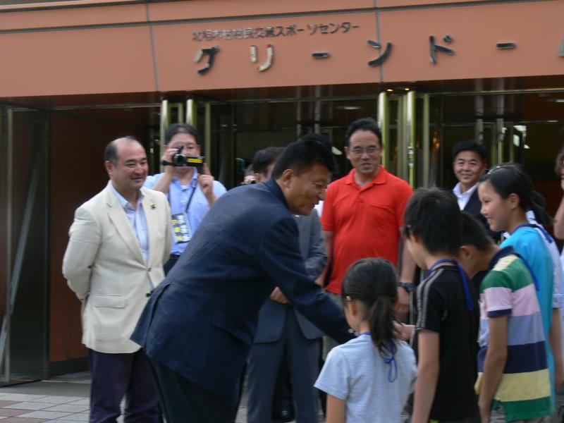 グリーンドームの前で子供たちに迎えられ笑顔の大臣
