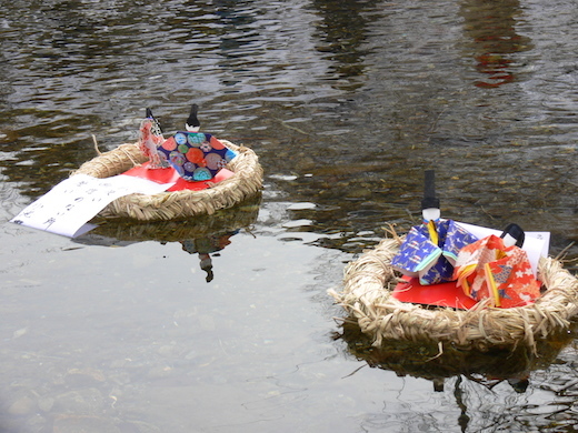 紙で作られたひな人形が、サンダワラに乗せられて川を流れる写真